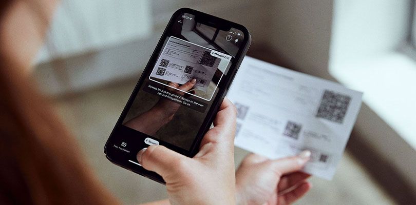 Eine Person hält ein Smartphone und scannt mit der Kamerafunktion einen QR-Code von einem ausgedruckten E-Rezept